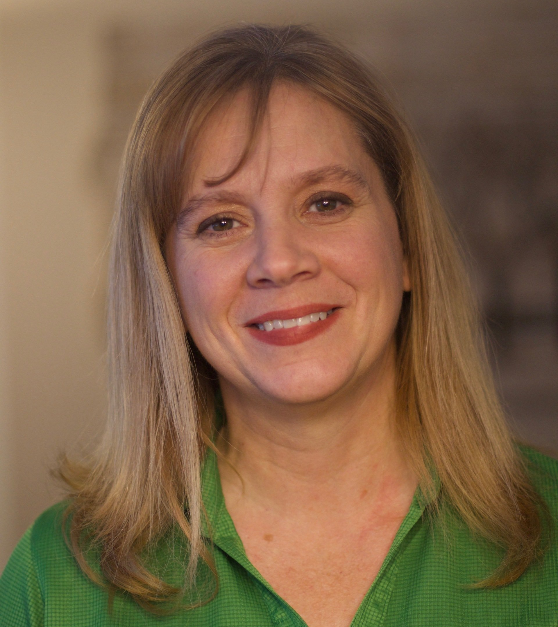 A woman in a green shirt is smiling for the camera.