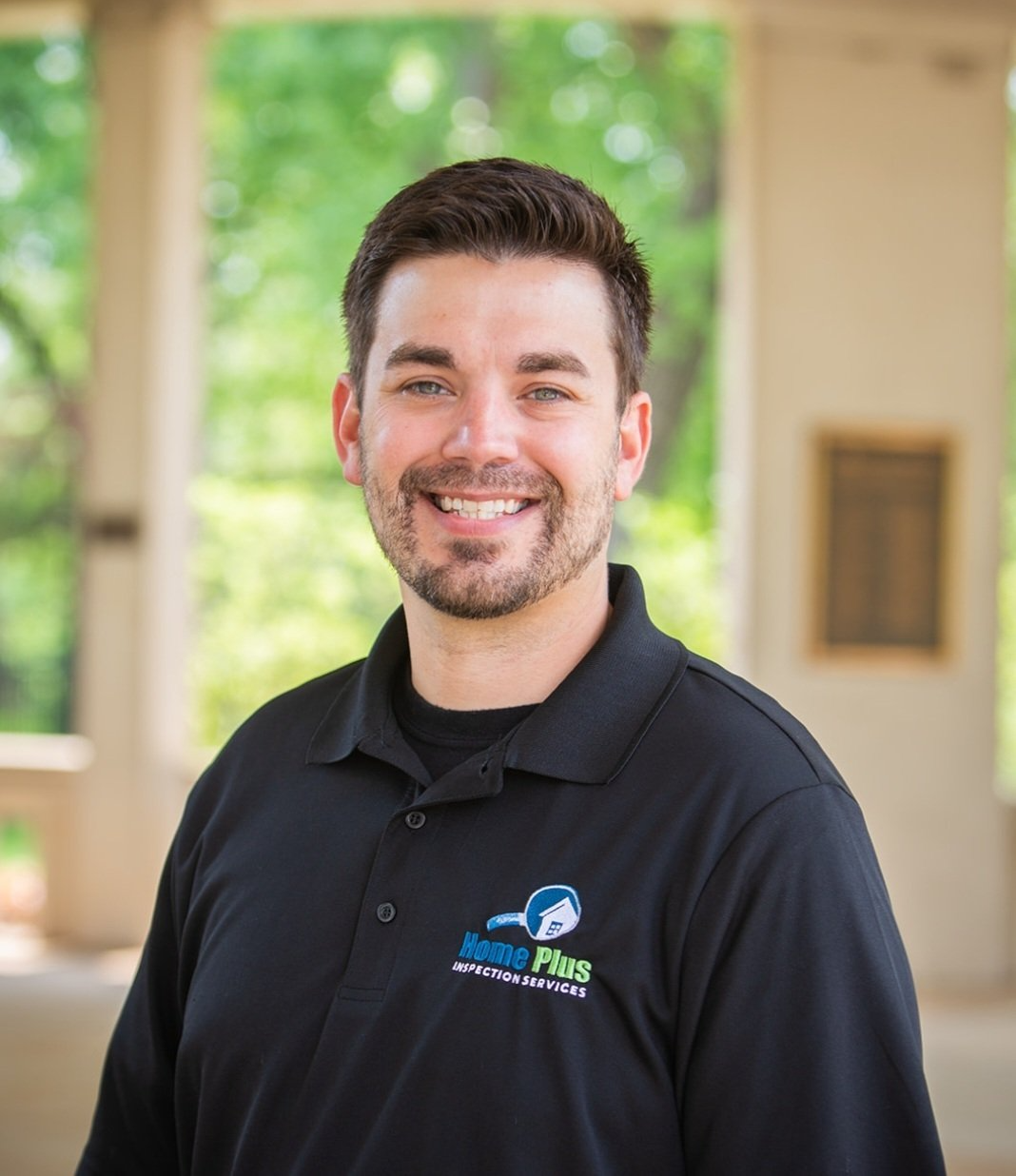 A man with a beard is wearing a black polo shirt and smiling.