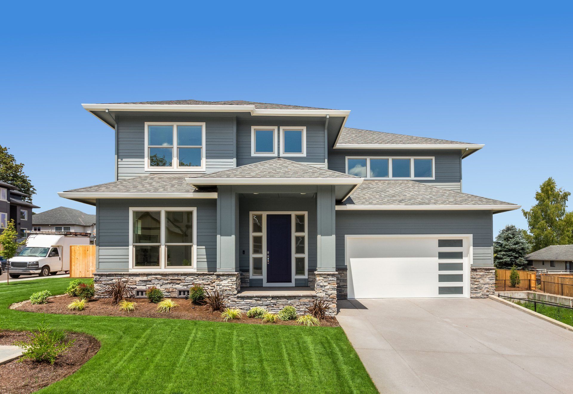 A large gray house with a white garage door is sitting on top of a lush green lawn.