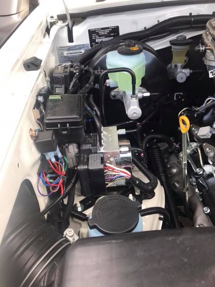 Engine compartment with various black boxes, wires, and fluid reservoirs. Primarily black and white.