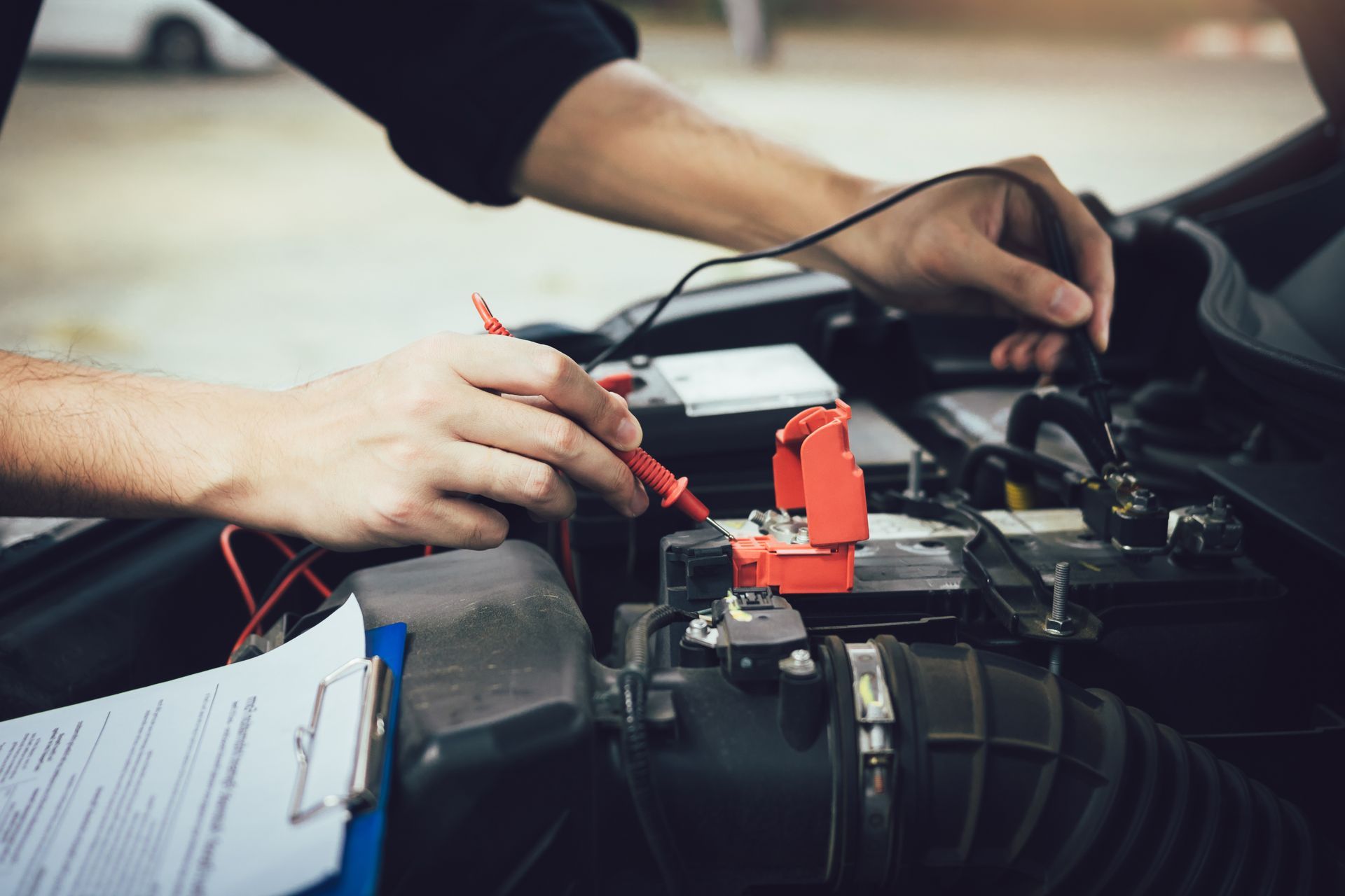 A man is using a multimeter to check the voltage of a car battery.