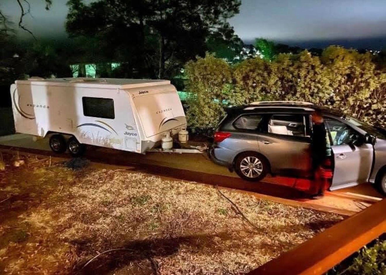 A silver SUV hitched to a white travel trailer parked in a driveway at night.