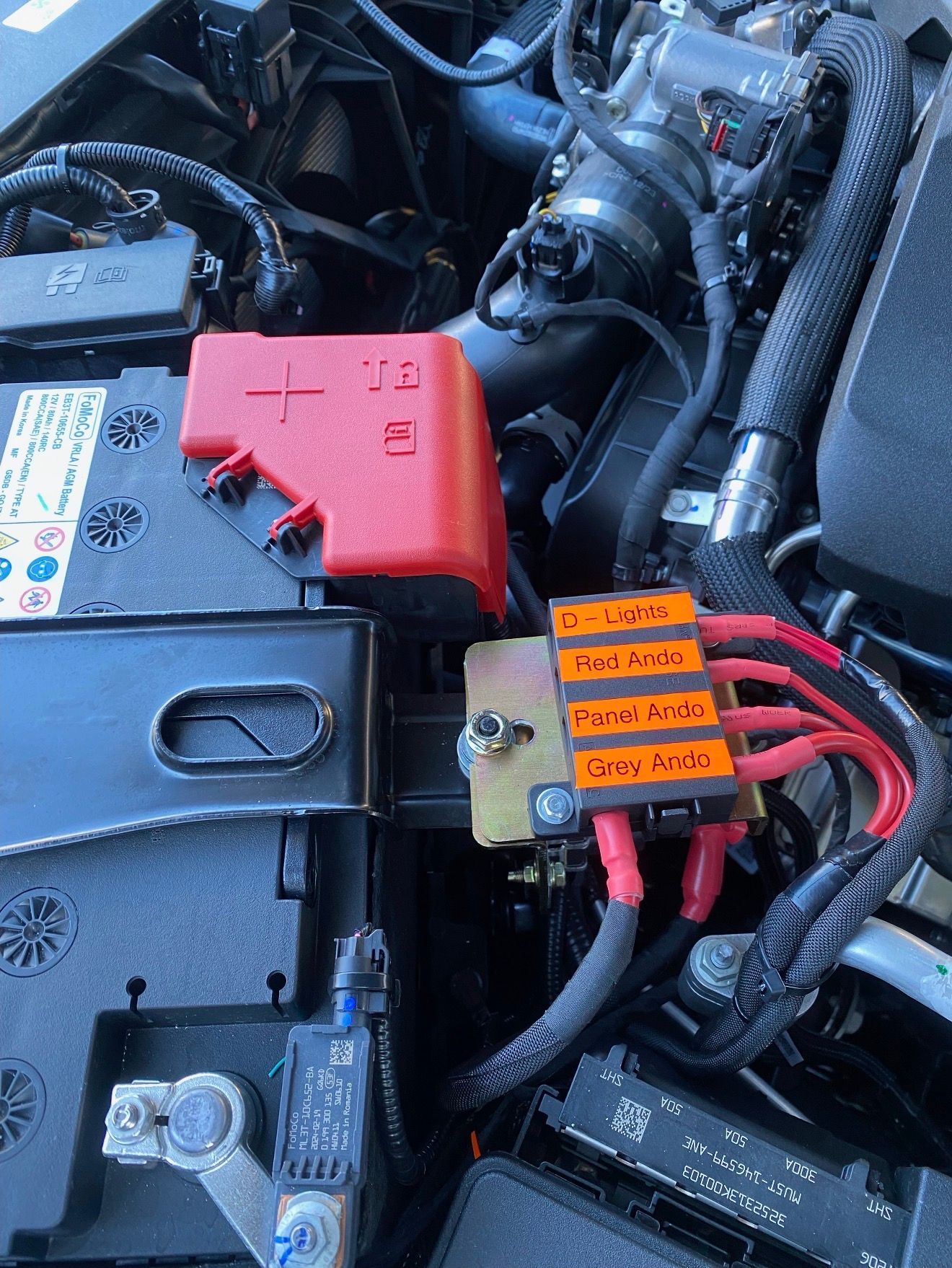 Car engine bay with battery, red fuse block, and wiring.