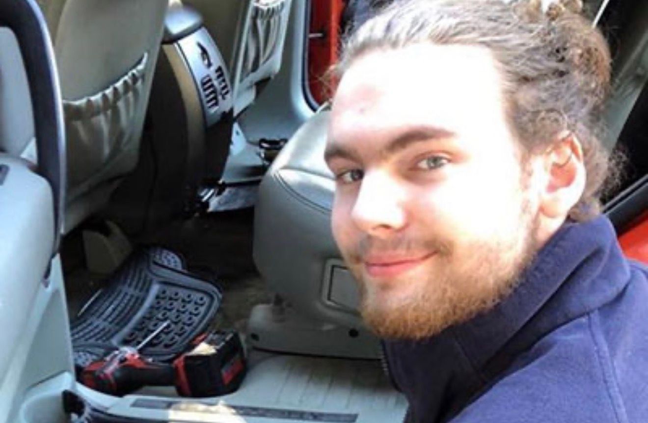Person smiling in a car’s back seat beside a laptop and cables
