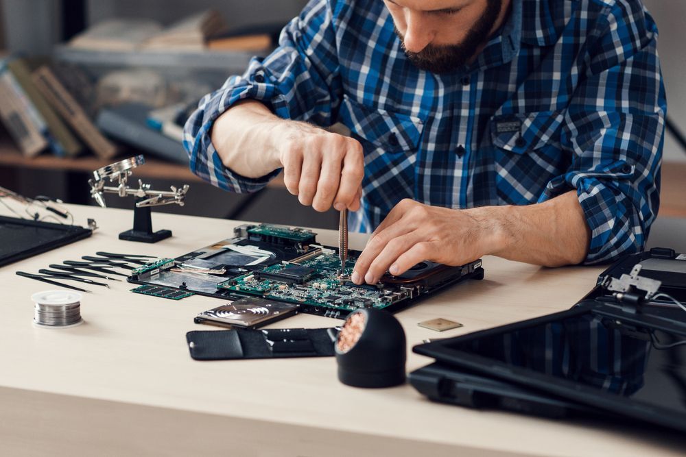 Man in Blue Plaid Shirt Repairs a Circuit Board With a Screwdriver at a Desk — Tech Aid In Sunshine Coast, QLD
