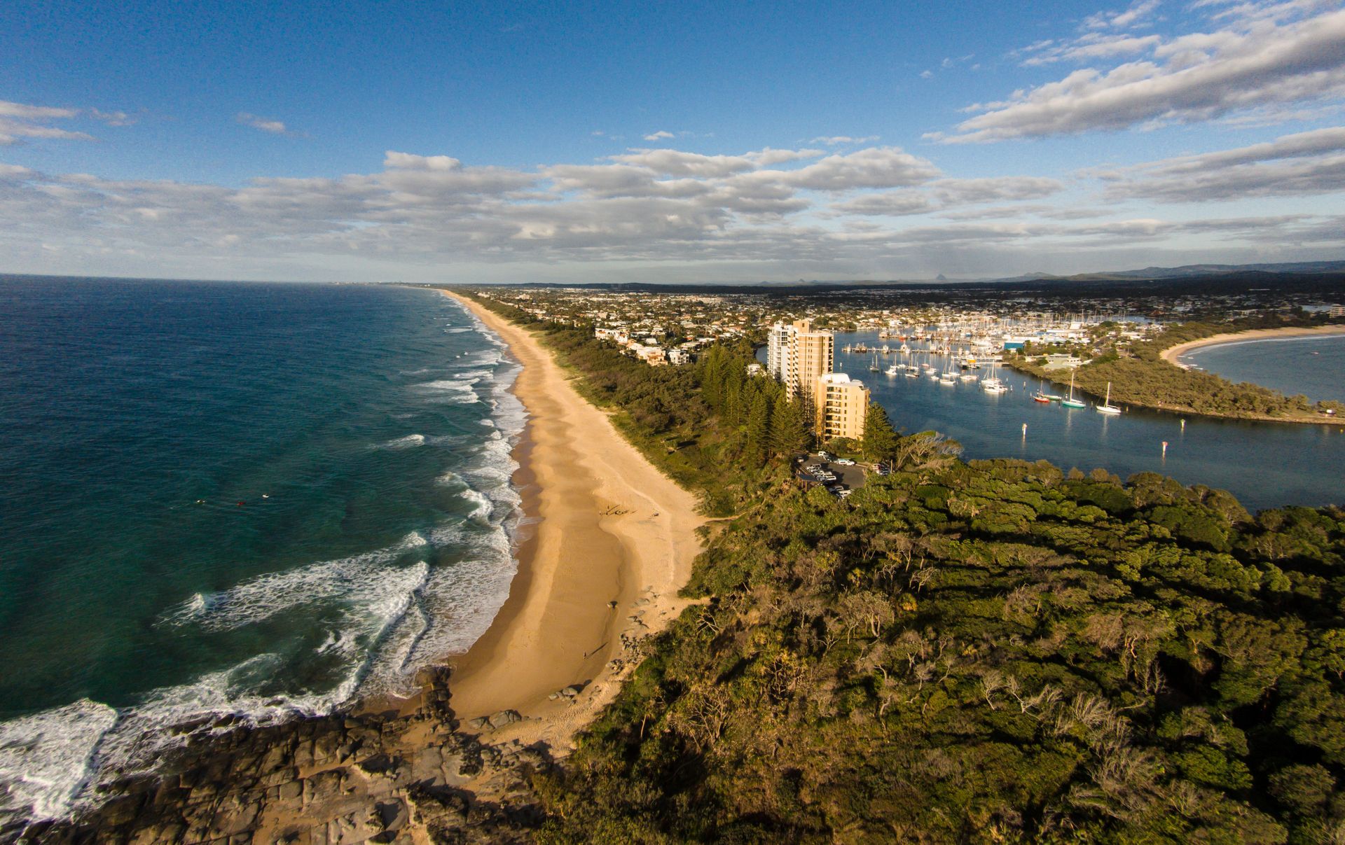 Aerial View of a Sandy Beach, Ocean Waves, and Green Coastal Forest Under a Blue Sky With Clouds — Tech Aid In Sunshine Coast, QLD