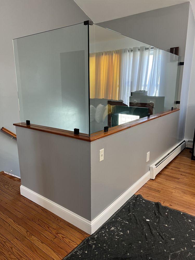 Glass partition panels installed on a half wall with wooden trim in a home interior with hardwood flooring.