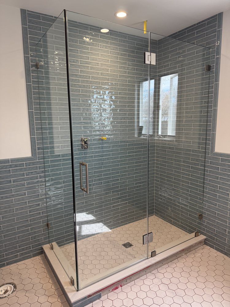 A glass-enclosed shower with blue subway tiles on the walls and white hexagonal floor tiles.