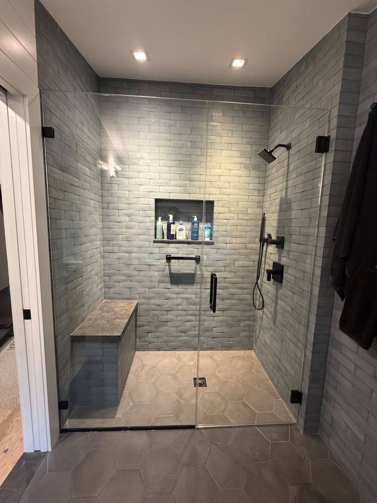 Modern walk-in shower with gray brick-style walls, hexagon floor tiles, a built-in bench, and black hardware.