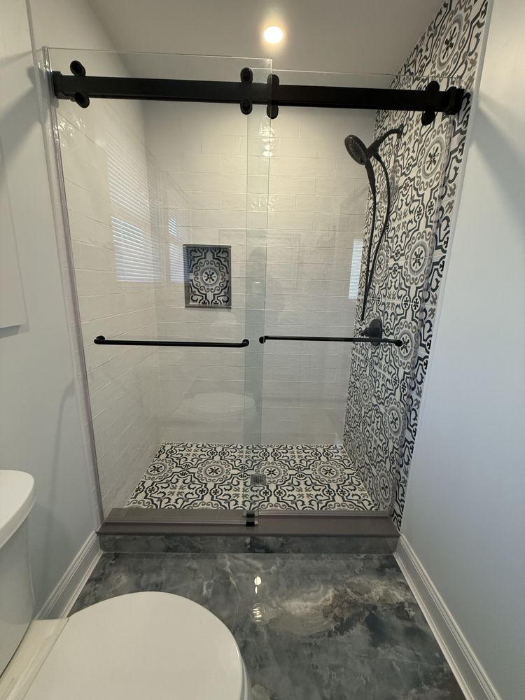 A walk-in shower with a black sliding glass door, patterned tile back wall and floor, and matte black shower fixtures.