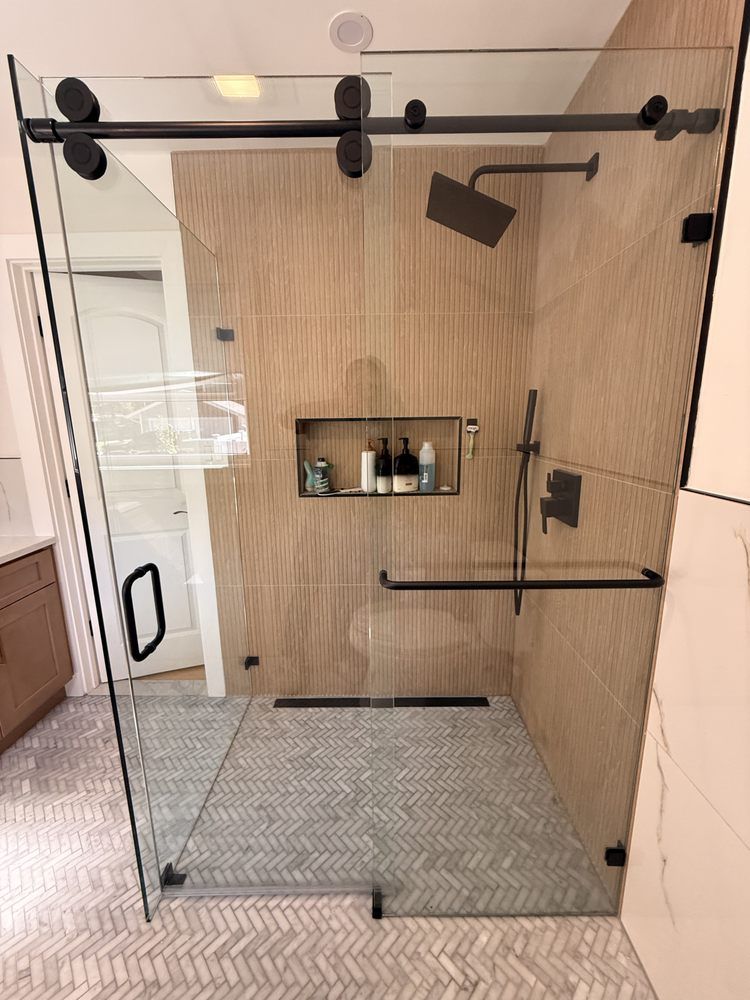 Modern walk-in shower with light wood-look tile, matte black sliding glass doors, a rainfall showerhead, and a wall niche.