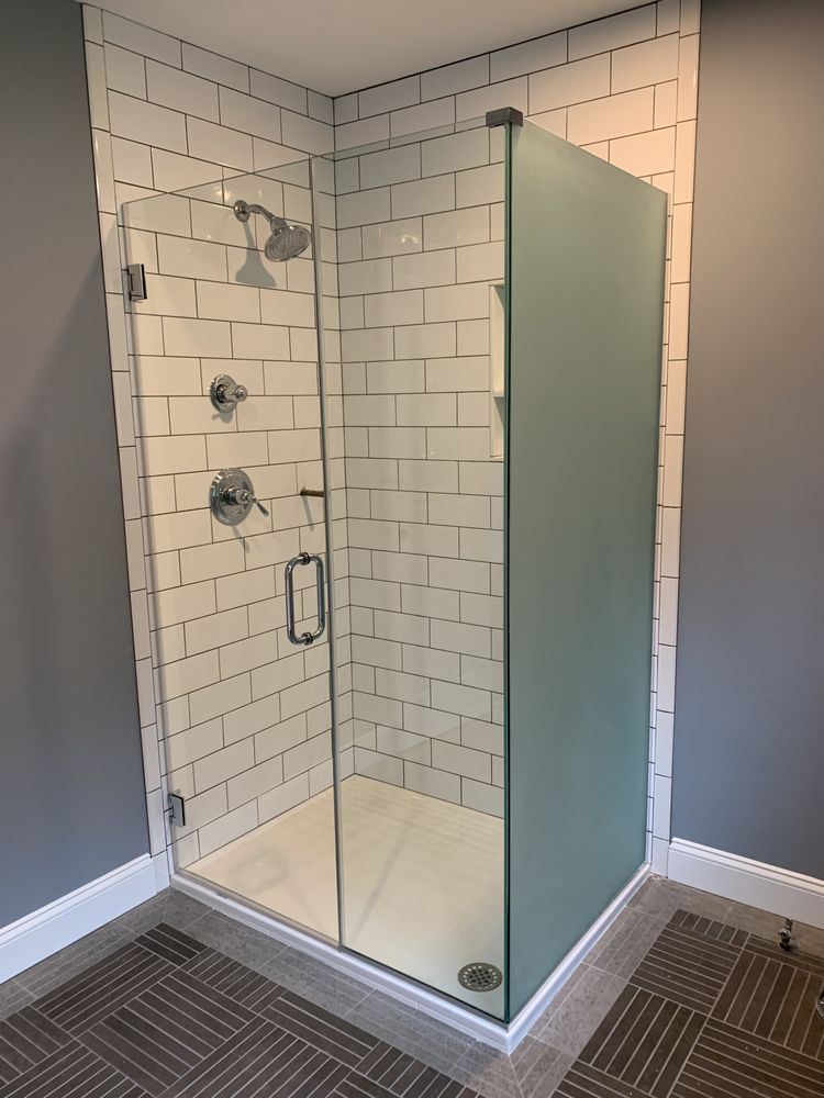 A glass shower enclosure with a door, chrome fixtures, and white subway tile walls, set in a room with gray walls.