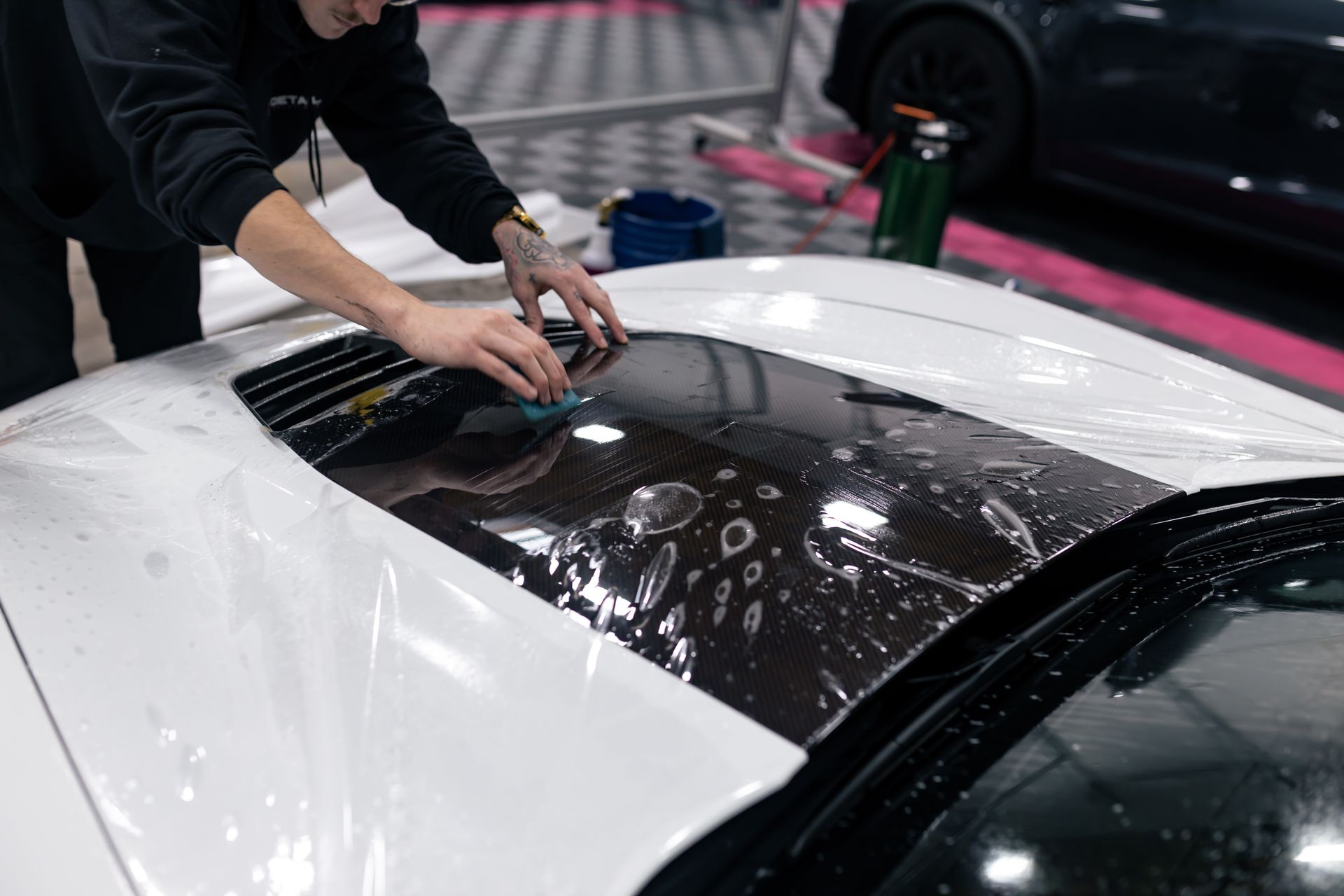 A man is cleaning the hood of a white car.