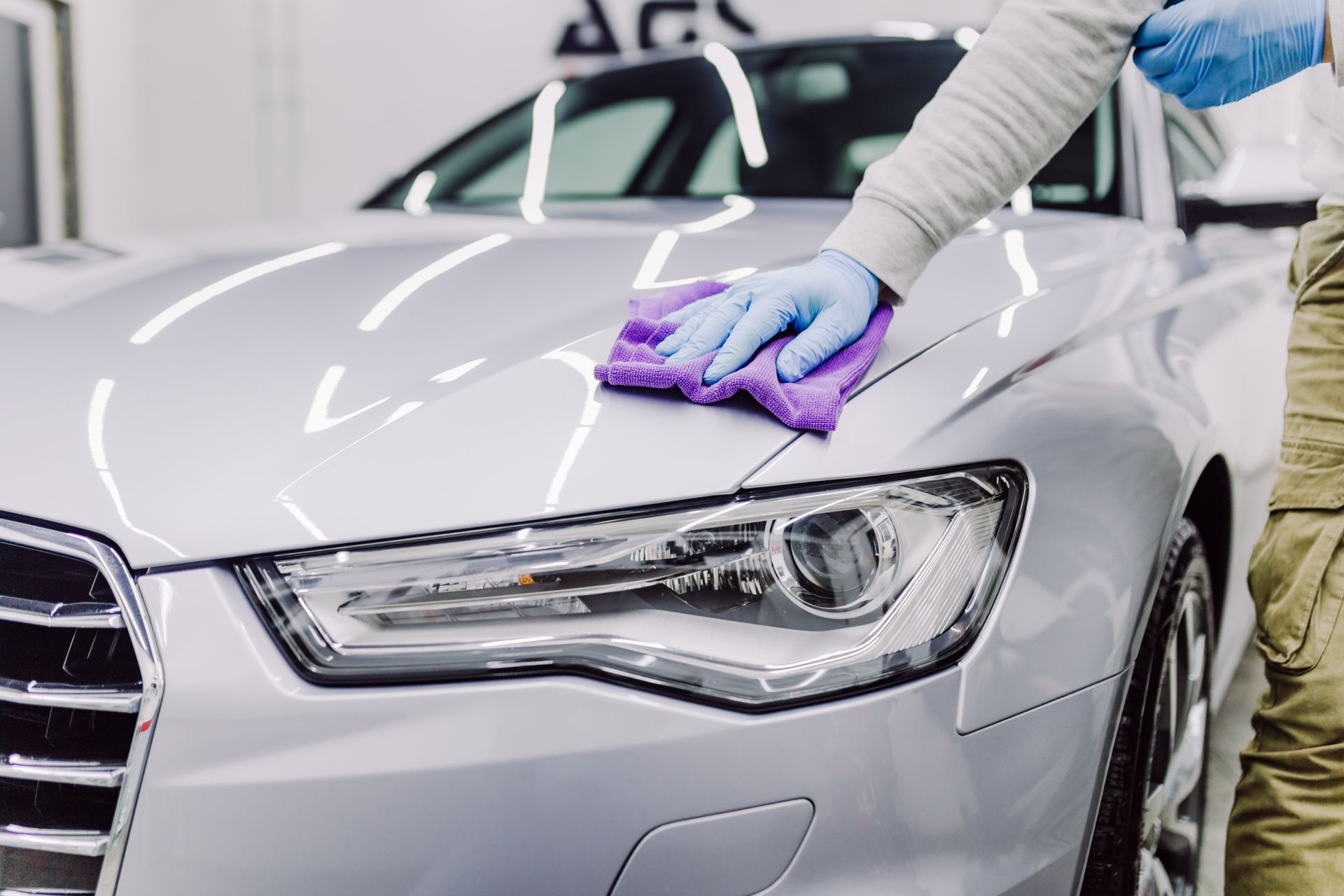 A man is cleaning a silver car with a purple cloth.