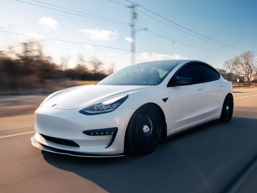 A white tesla model 3 is driving down a road.