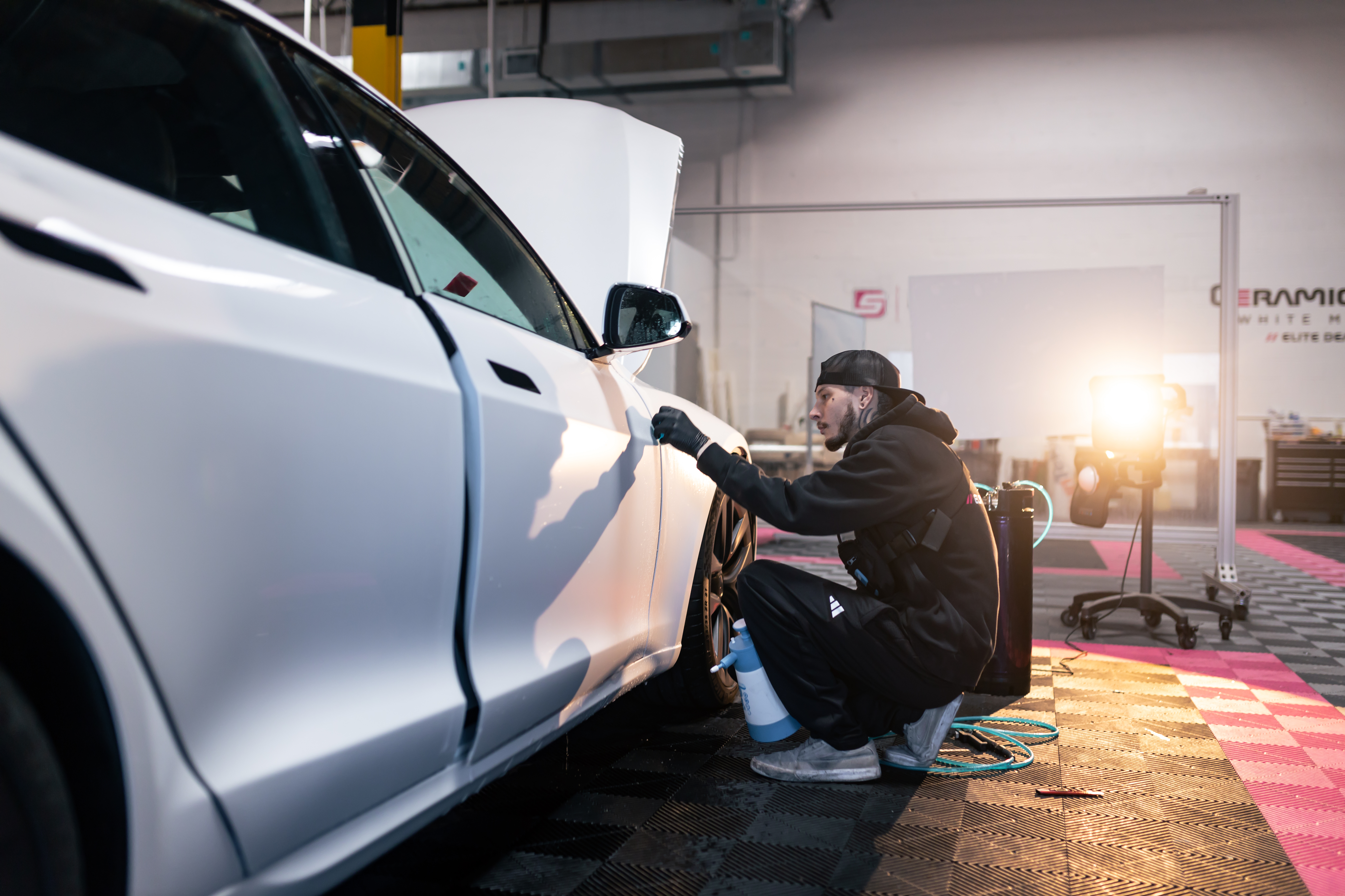 A man is sitting on a stool working on a car in a garage.