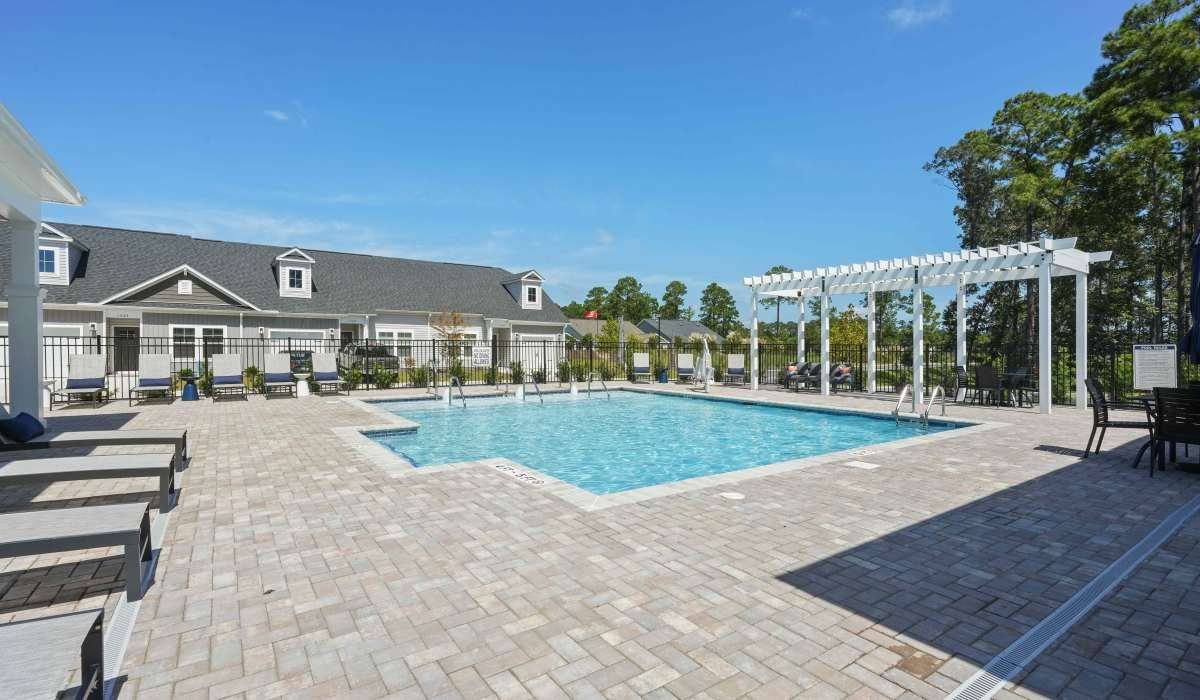 A swimming pool with white pergola, loungers, and a building on a sunny day.