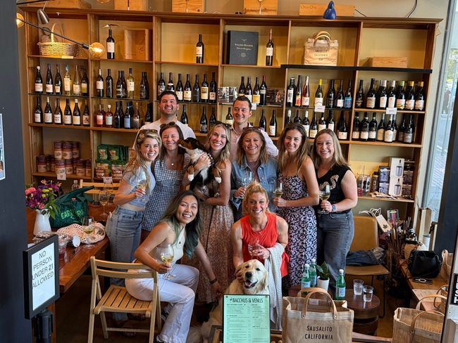 A group of people posing for a picture in front of shelves of wine bottles