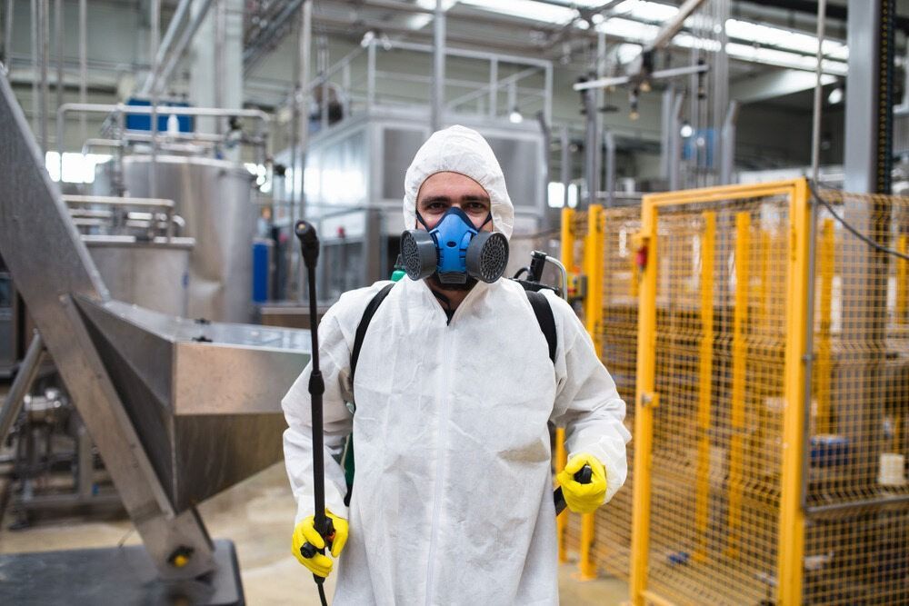 A Man In A Protective Suit And Mask Is Spraying Chemicals In A Factory — ASAP Pest Control in Sunnybank Hills, QLD