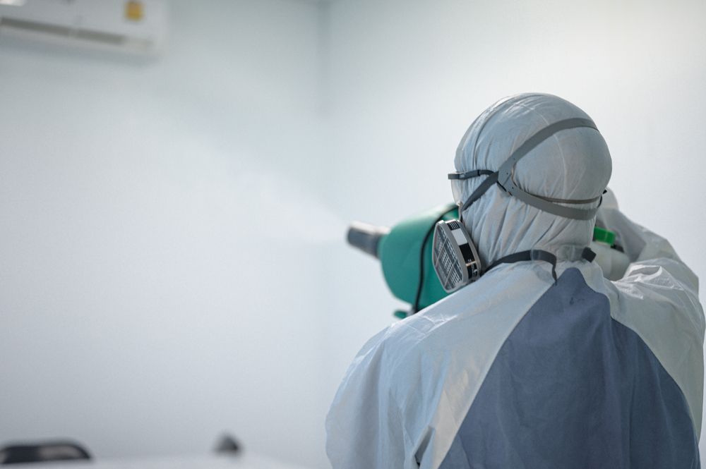 A Man In A Protective Suit Is Spraying A Room With A Sprayer — ASAP Pest Control in Canungra, QLD