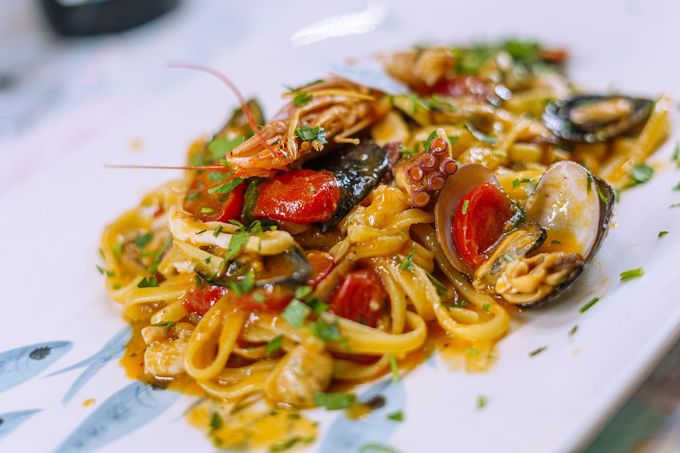 Pasta ai frutti di mare con gamberi, cozze, polpo, pomodori ed erbe aromatiche su un piatto bianco.
