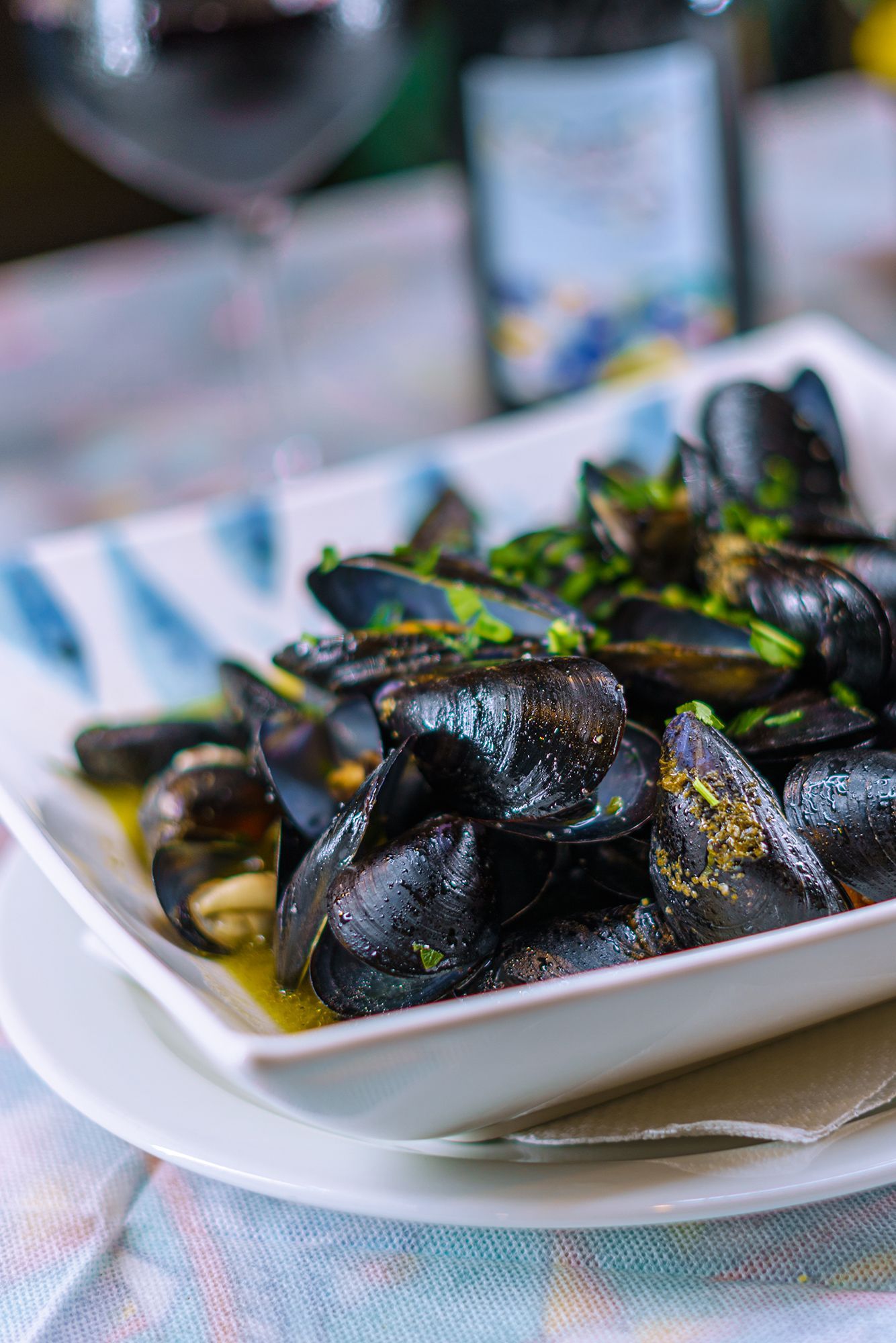 Cozze al vapore in una ciotola bianca, guarnite con prezzemolo, su un tavolo con del vino.