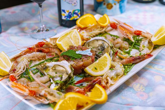 Piatto di frutti di mare con gamberi, ostriche e fette di limone su un tavolo con una bottiglia di vino.