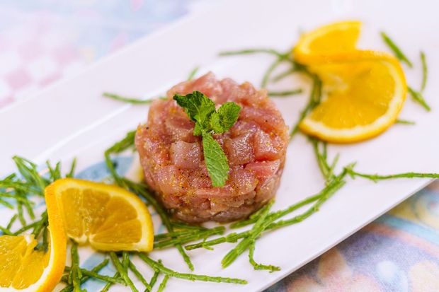 Tartare di tonno crudo su un piatto bianco, guarnita con fette d'arancia e verde.