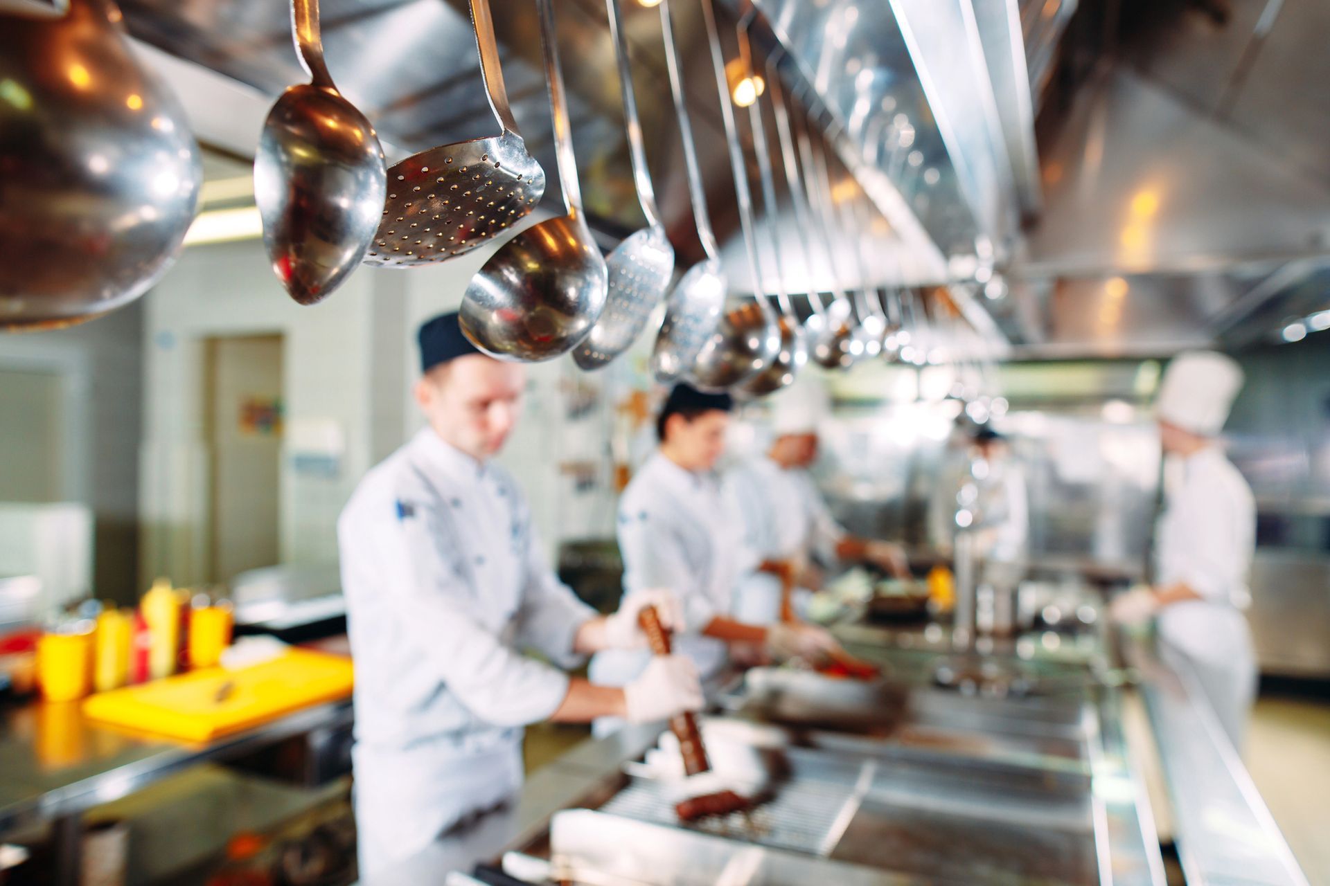 Chef al lavoro in una luminosa cucina professionale, con pentole di rame appese e ripiani in acciaio inossidabile.