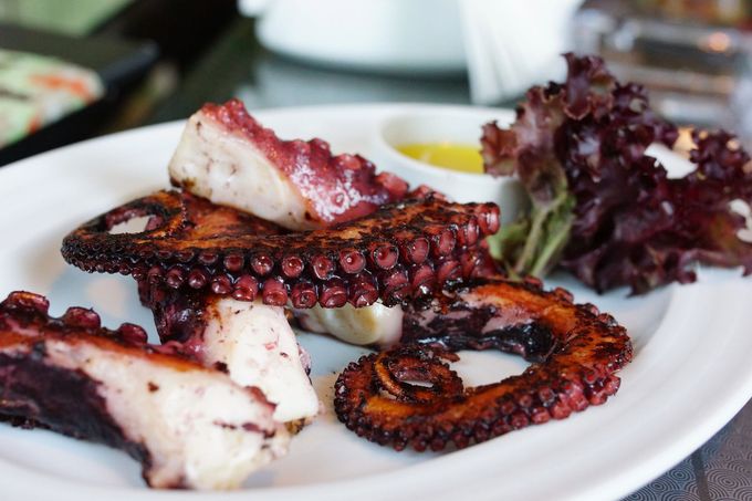 Tentacoli di polpo grigliati su un piatto bianco con verdure e salsa.