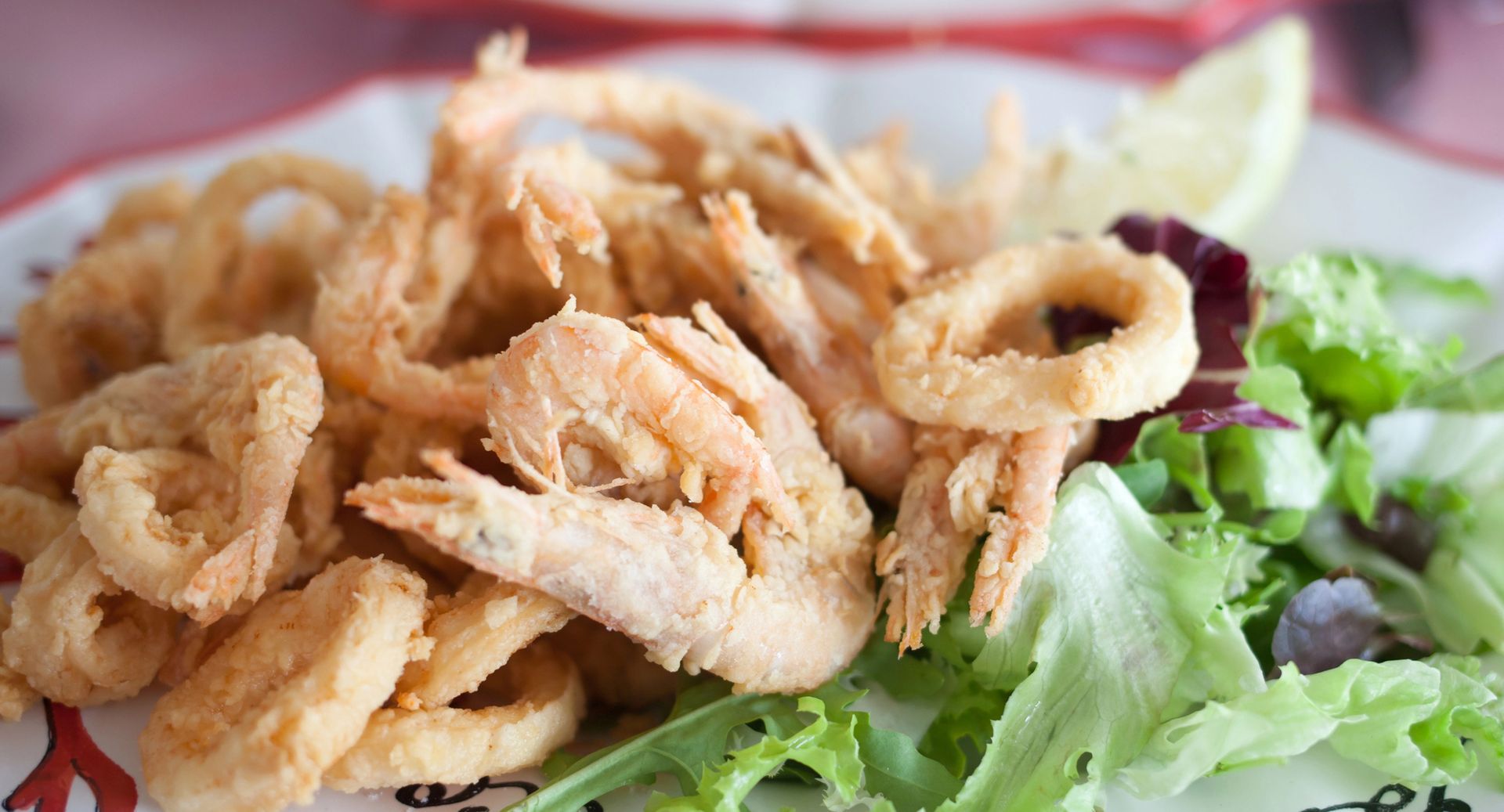 Piatto di calamari fritti croccanti su un letto di lattuga con guarnizione di limone.