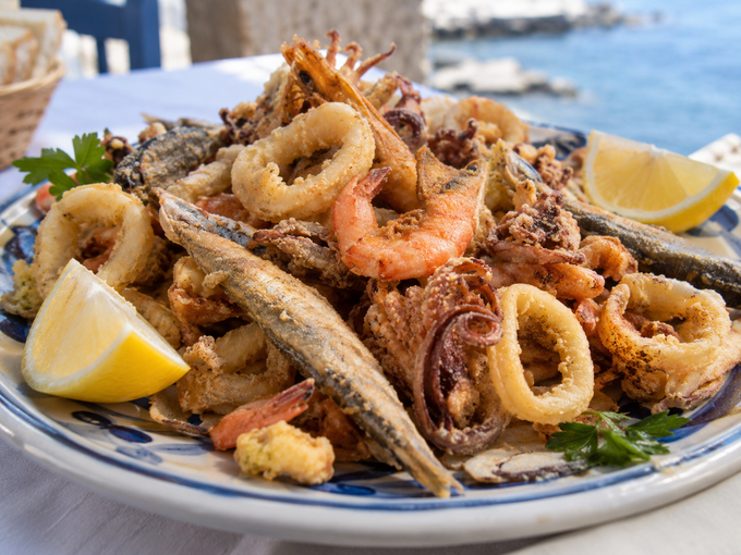 Piatto di frutti di mare fritti con spicchi di limone su un tavolo in riva all'acqua.