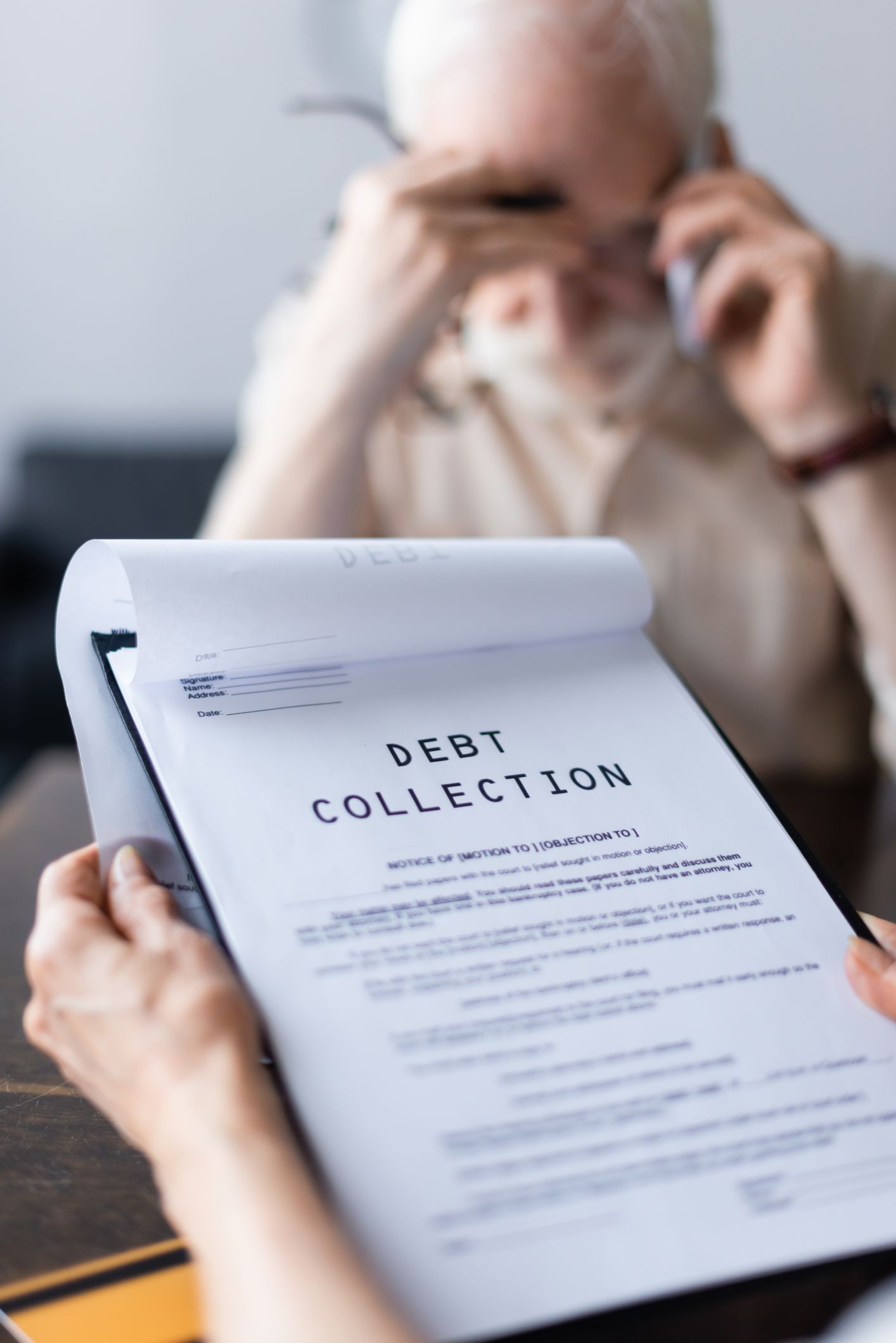 Focus of woman holding papers with debt collection lettering near husband talking on the phone.