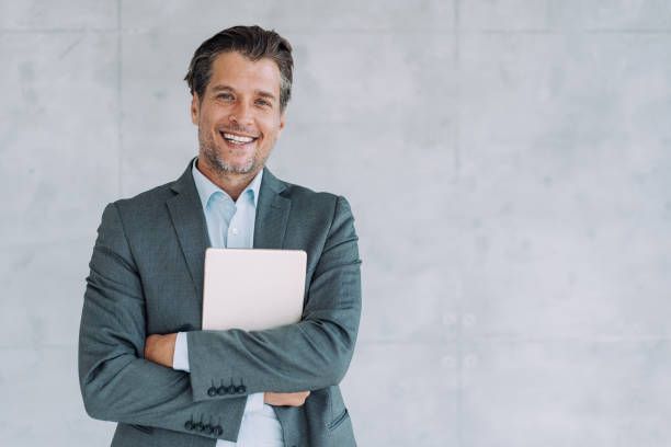 A Man In A Suit Is Holding A Laptop And Smiling. — Savannah, GA — Abercorn Insurance Agency