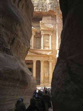 A group of people are walking through a canyon towards a building.