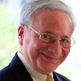 A man wearing glasses and a suit and tie is smiling.