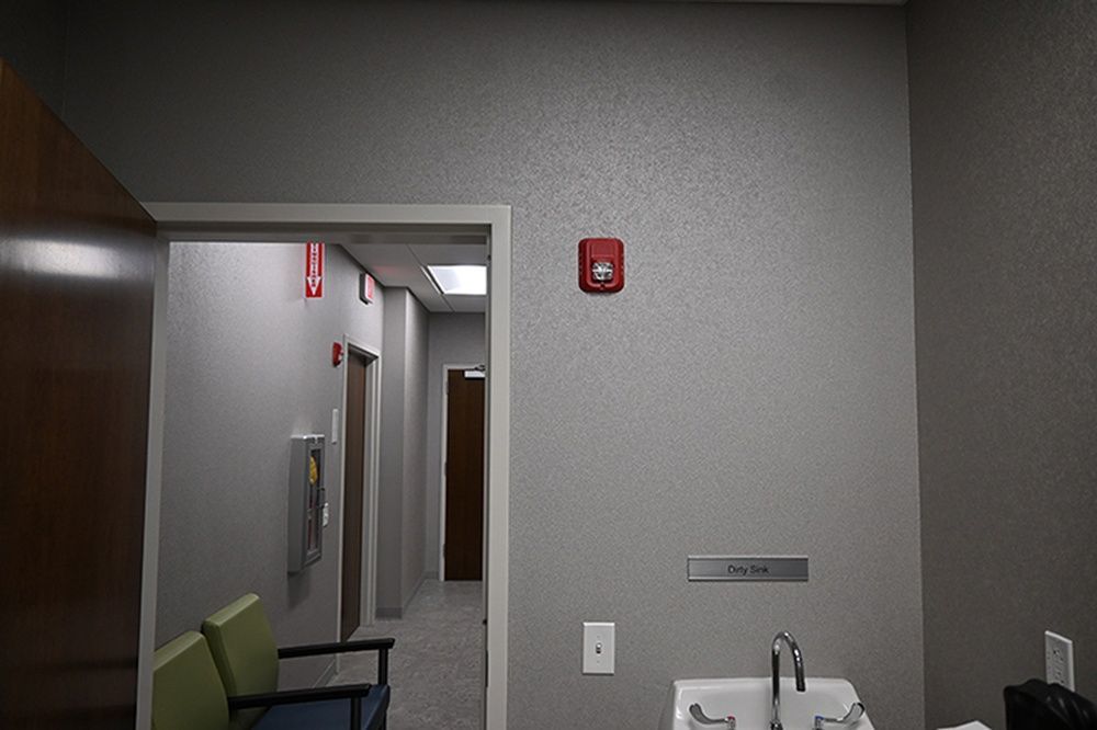 A waiting room with a sink and chairs and a fire alarm on the wall.