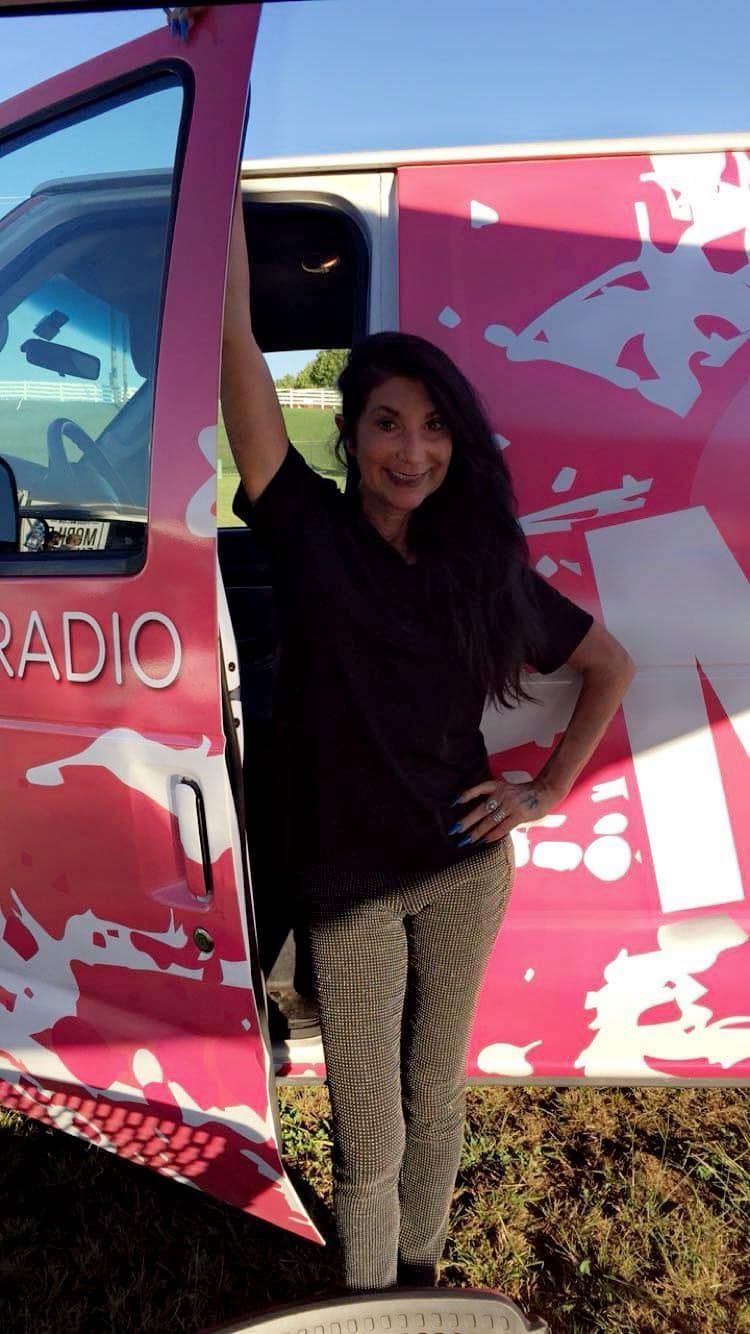 A woman is standing in front of a pink radio van