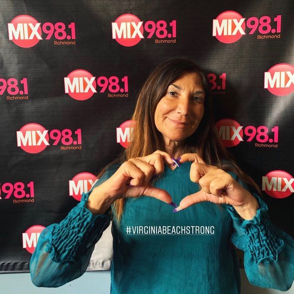 A woman making a heart with her hands in front of a mix 98.1 banner