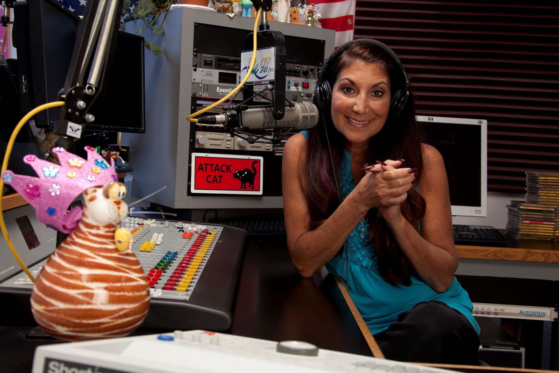 A woman wearing headphones sits at a desk in front of a sign that says kitty cat