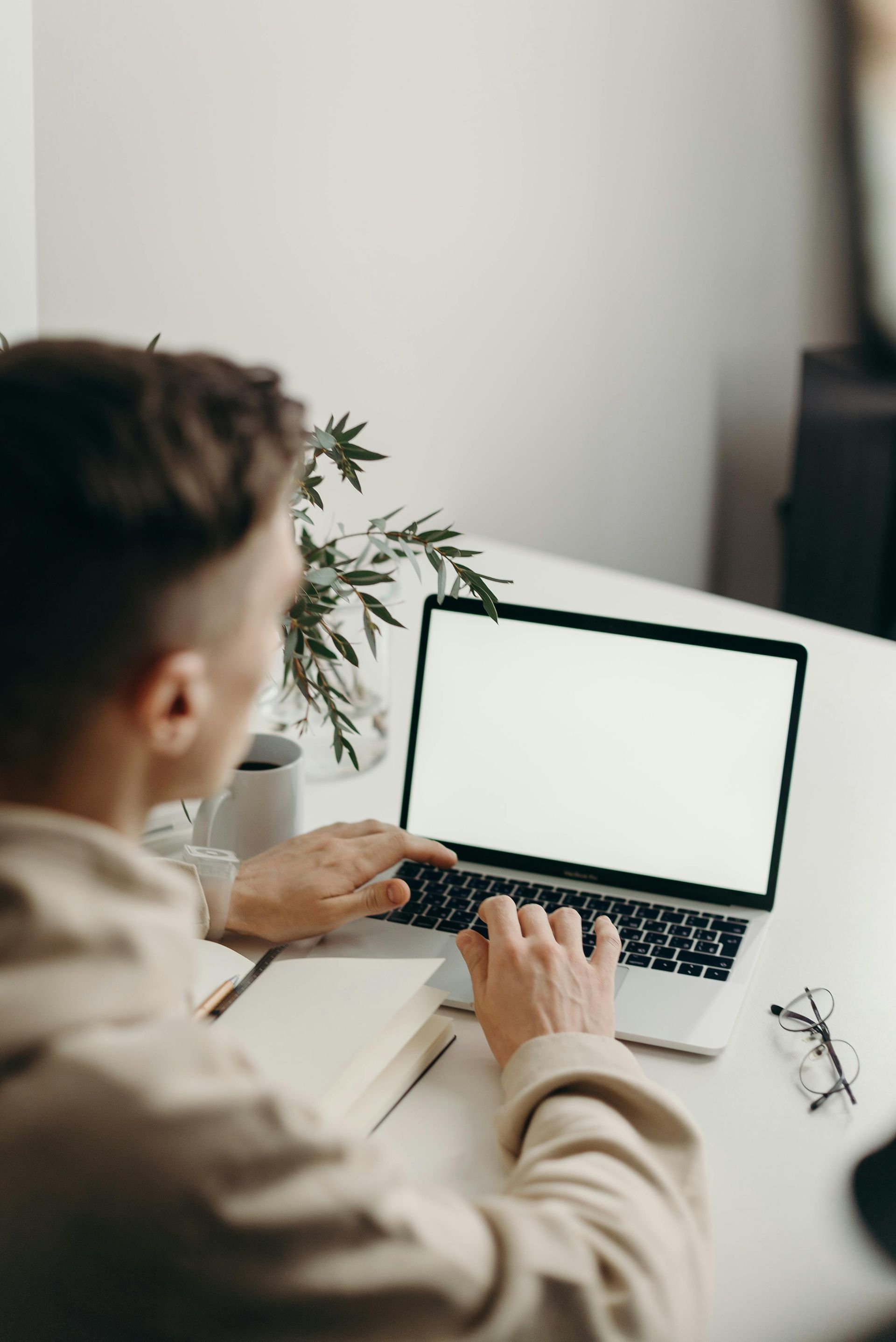 A man is typing on a laptop computer with a white screen.