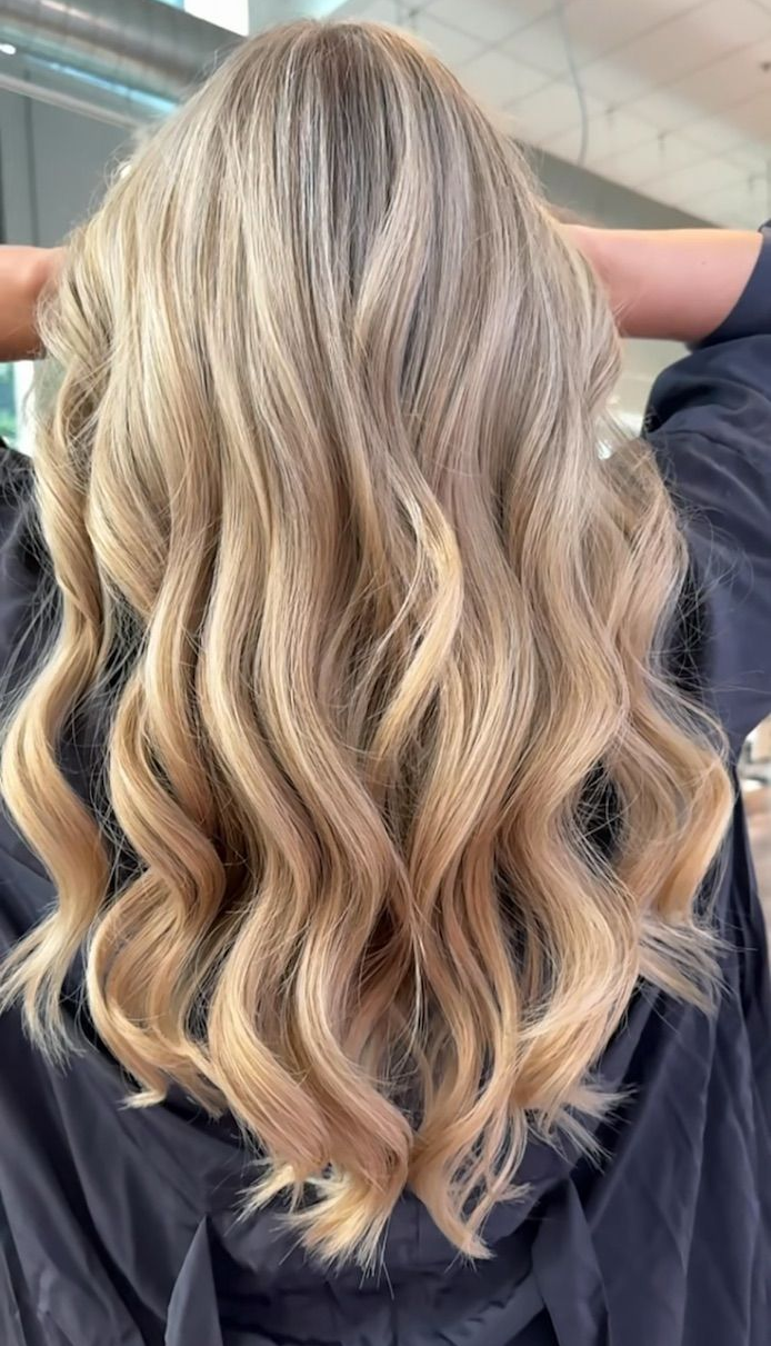 Woman with wavy, blonde balayage and bangs, in a salon.