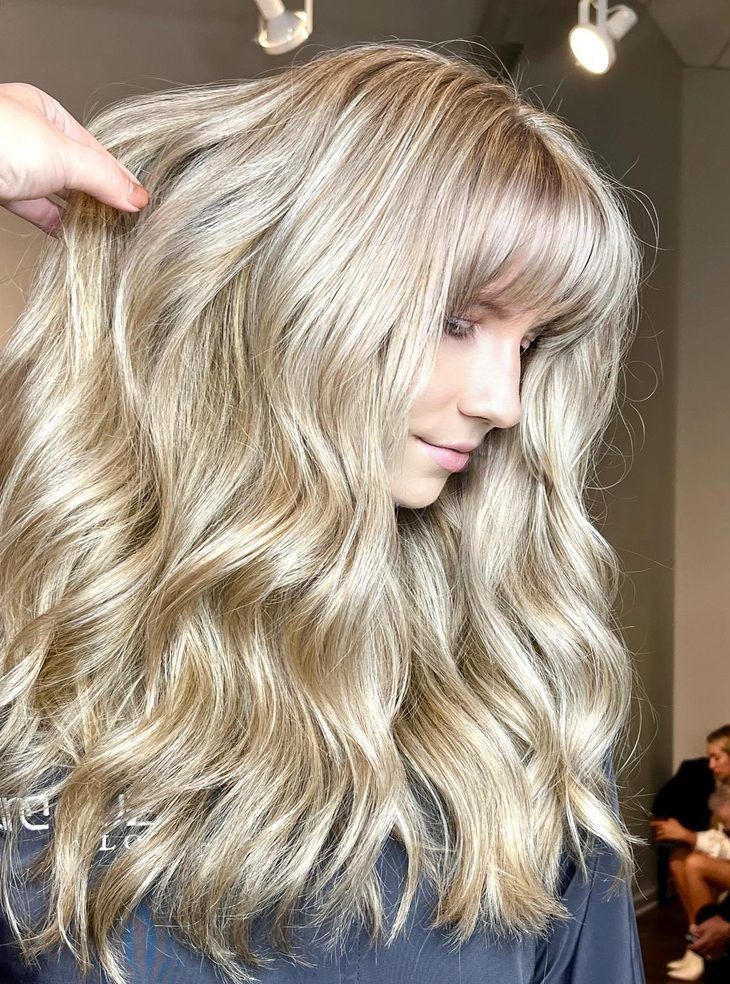 Woman with wavy, blonde balayage and bangs, in a salon.