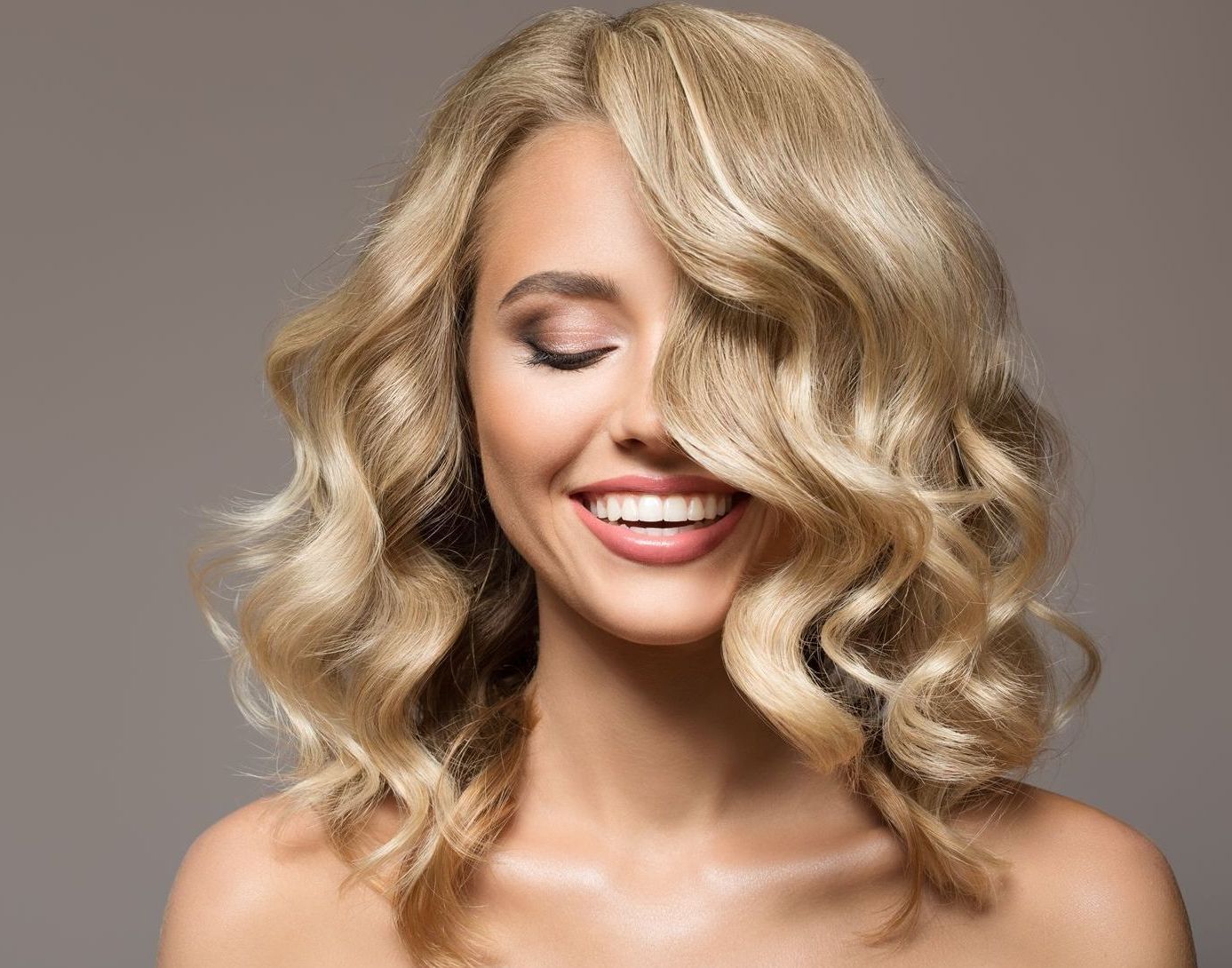 Blonde woman with wavy hair smiling, after hair coloring appointment, eyes closed.