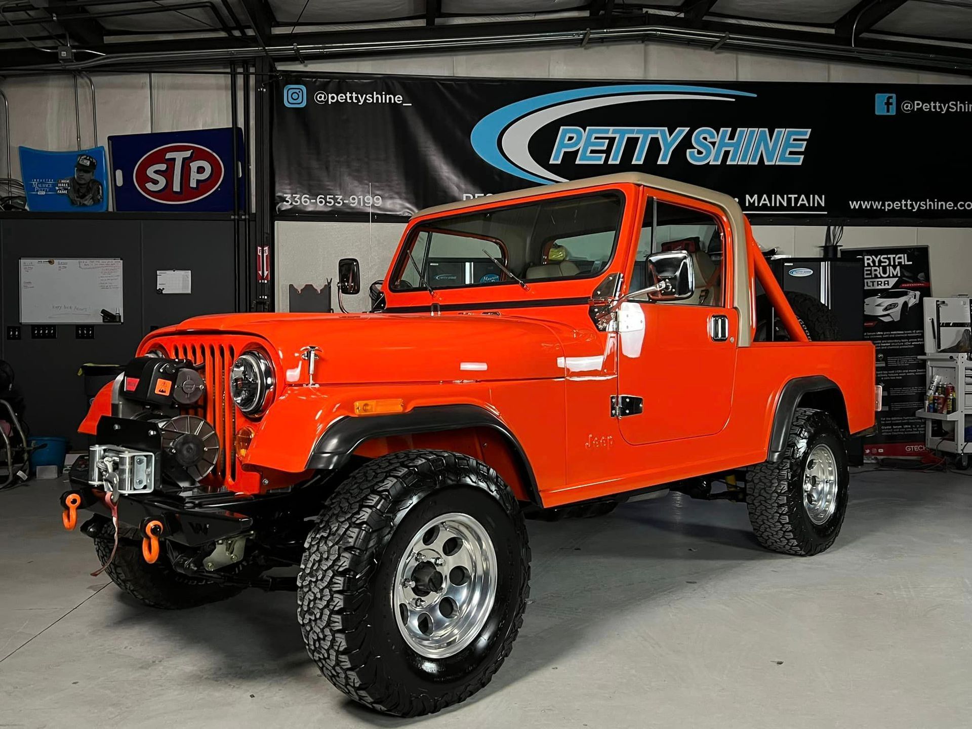 Bright orange Jeep CJ with a white roll cage parked inside a garage.