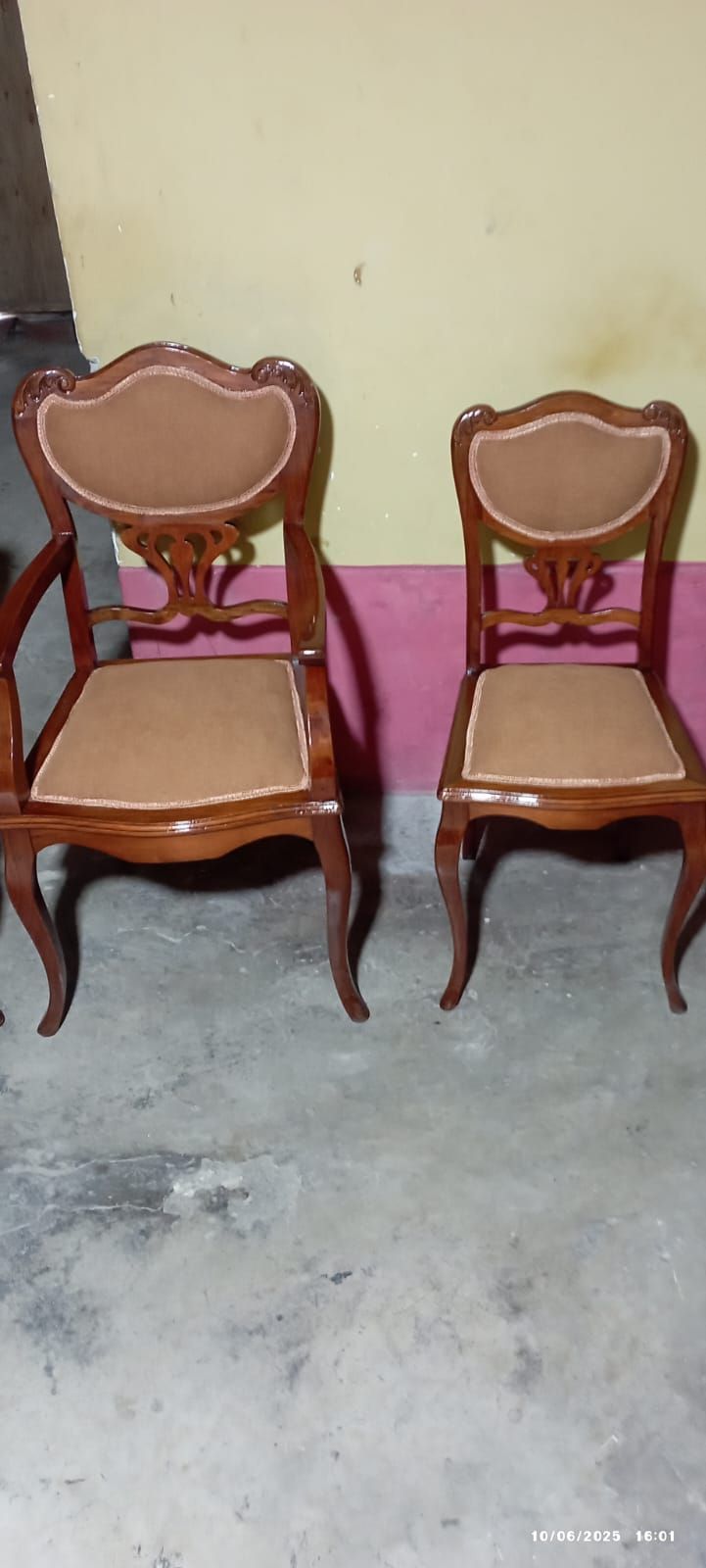 Dos sillas de madera ornamentadas con asientos y respaldos marrones, colocadas contra una pared de dos tonos.