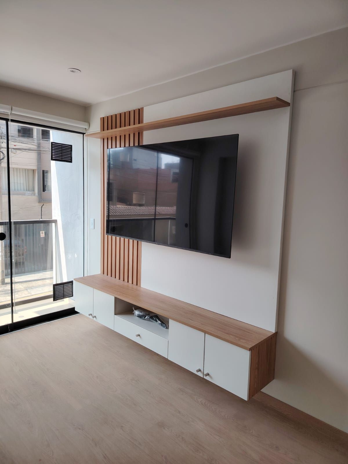Moderno centro de entretenimiento en madera y blanco con TV montada sobre un mueble flotante.