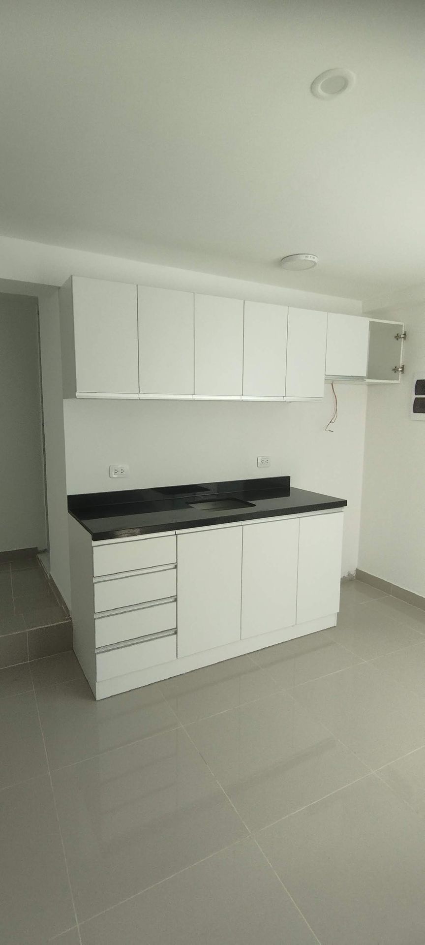 Gabinetes de cocina y encimeras blancas en una habitación con pisos y paredes de colores claros.