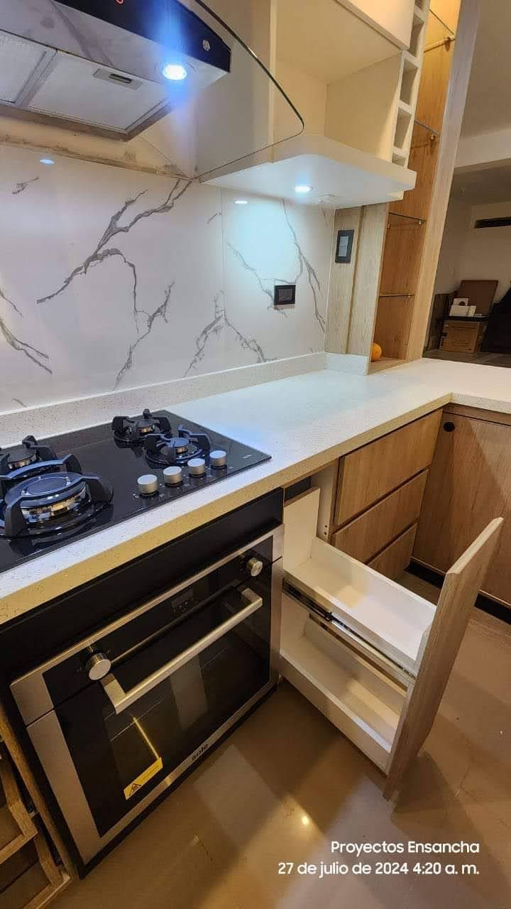 Cocina moderna con estufa y horno negros, encimeras blancas y gabinetes de madera clara.