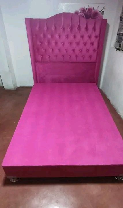 Cama tapizada en color rosa con cabecero capitoné sobre suelo marrón.